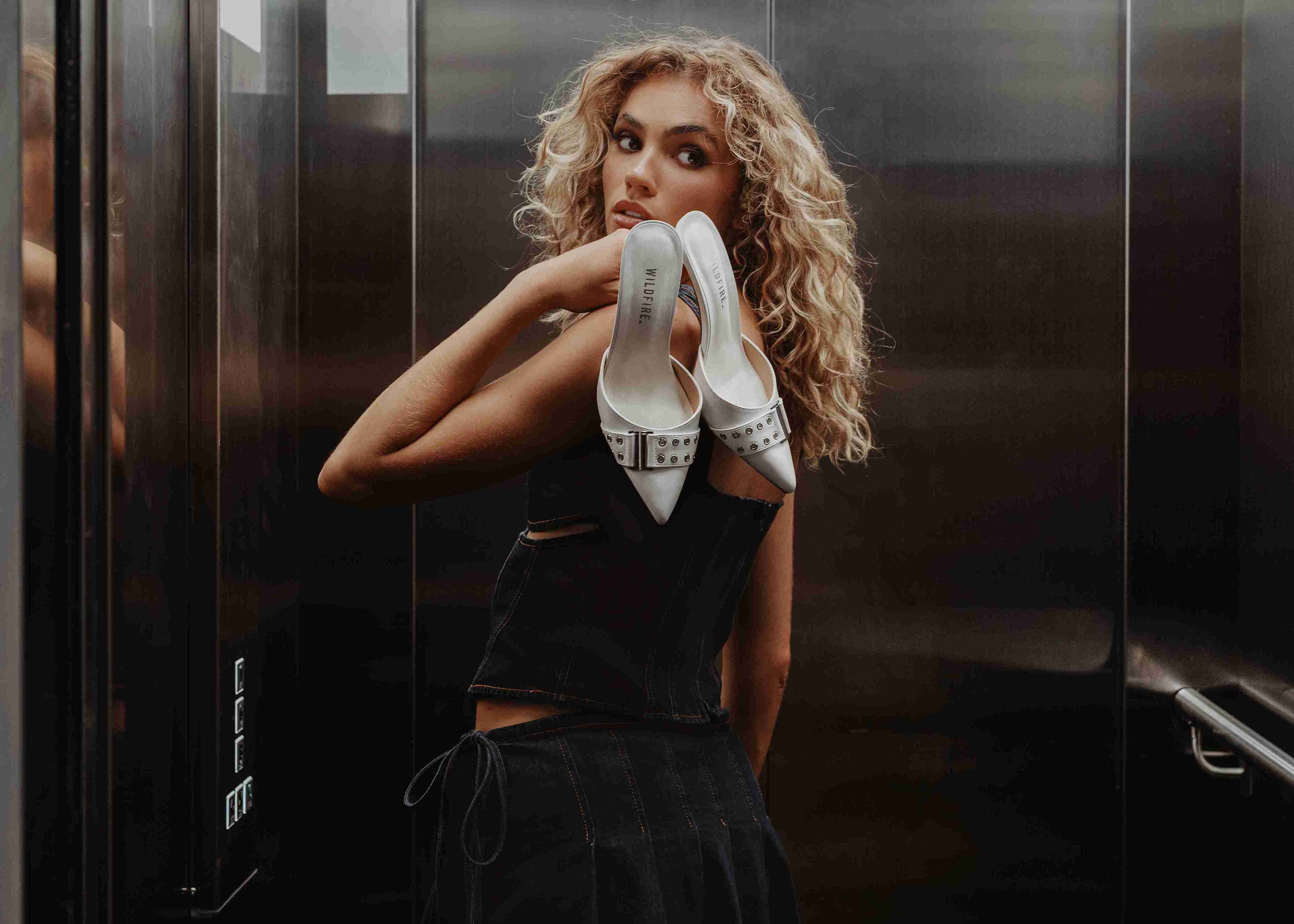 Female holding a paid of shoes behind her.
